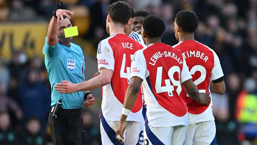 Referee Michael Oliver drops a yellow card before showing Myles Lewis-Skelly a red one (©Shaun Botterill/Getty Images)